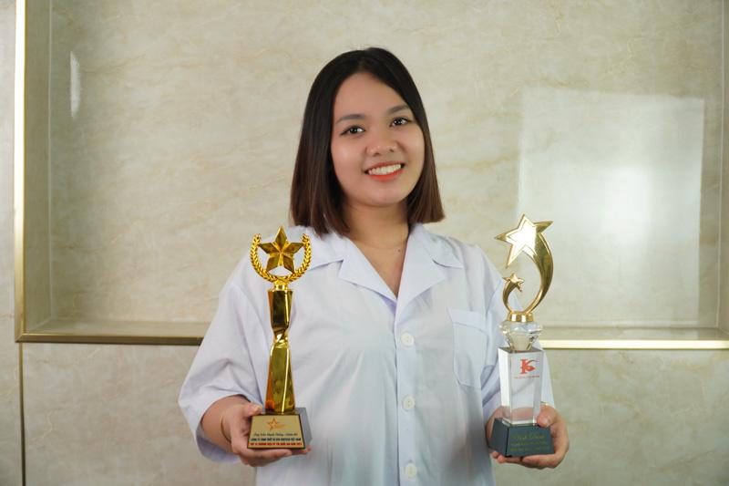 Hình ảnh sau khi xóa xăm bằng công nghệ Laser hiện đại 19 Master Artist Phạm Thanh Tâm tại Thẩm Mỹ Rio, cầm hai chiếc cúp vàng và bạc biểu trưng cho thành tích nghề nghiệp.