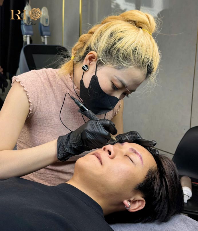 Artist Thuy Tien expertly performing a masterful eyebrow feathering tattoo at Rio Beauty Clinic.