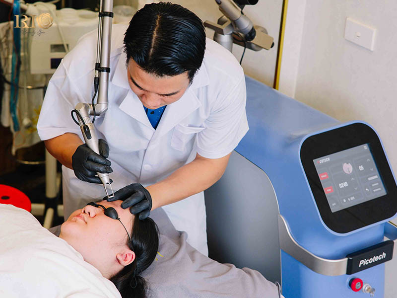 A trained technician at a laser tattoo removal clinic near me in Hanoi performs a precise eyebrow tattoo removal treatment on a patient using a specialized laser handpiece.