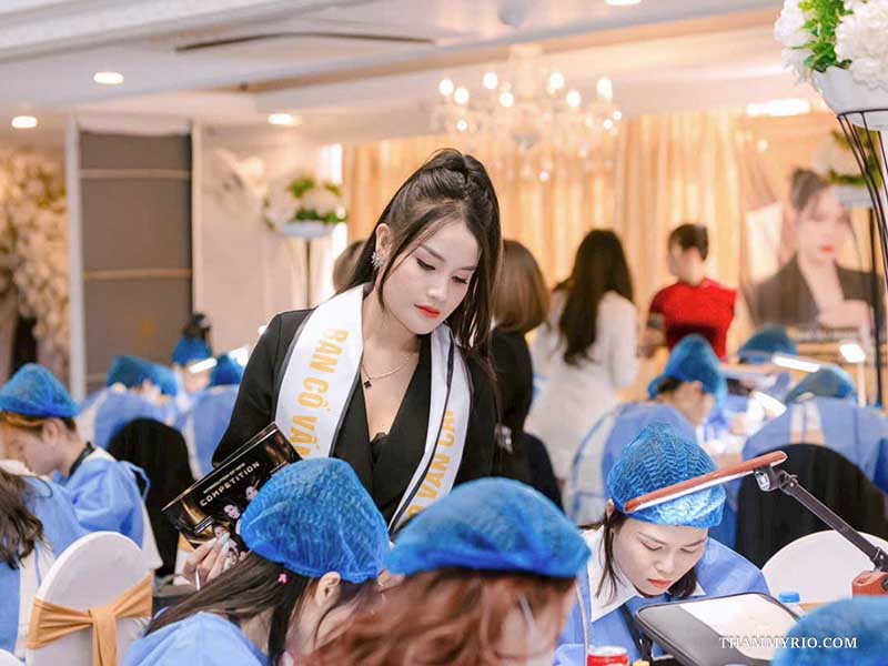 Giảng viên Kiều Nhi Thẩm mỹ Rio đeo băng rôn Ban cố vấn đang tận tình đứng lớp hướng dẫn học viên thực hành kỹ thuật phun xăm thẩm mỹ.