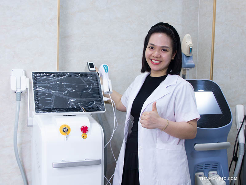 Laser tattoo removal specialist smiling and giving a thumbs up next to professional removal equipment.