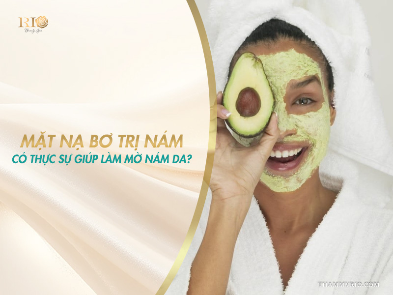 Người phụ nữ vui vẻ đắp mặt nạ bơ và cầm nửa quả bơ tươi che một bên mắt trên banner giải đáp mặt nạ bơ trị nám