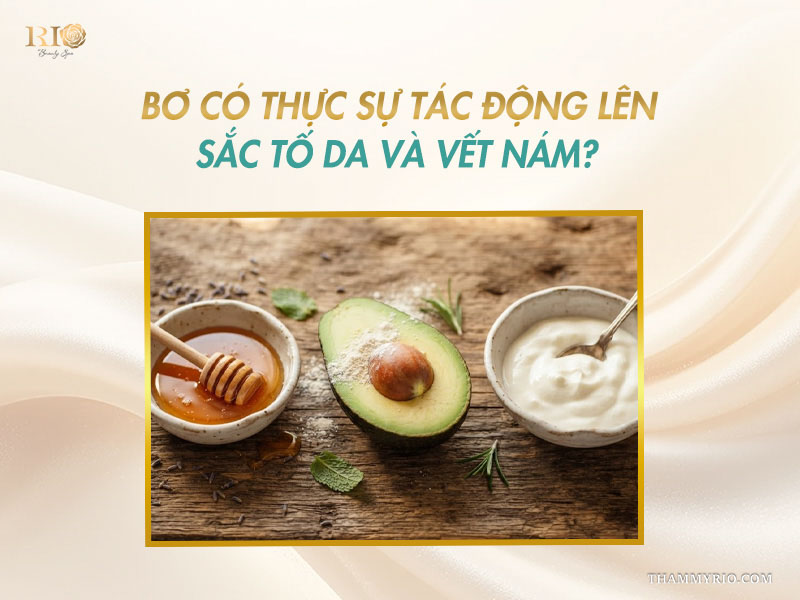 Nửa quả bơ tươi đặt giữa hai bát nhỏ đựng mật ong nguyên chất và sữa chua không đường trên mặt bàn gỗ